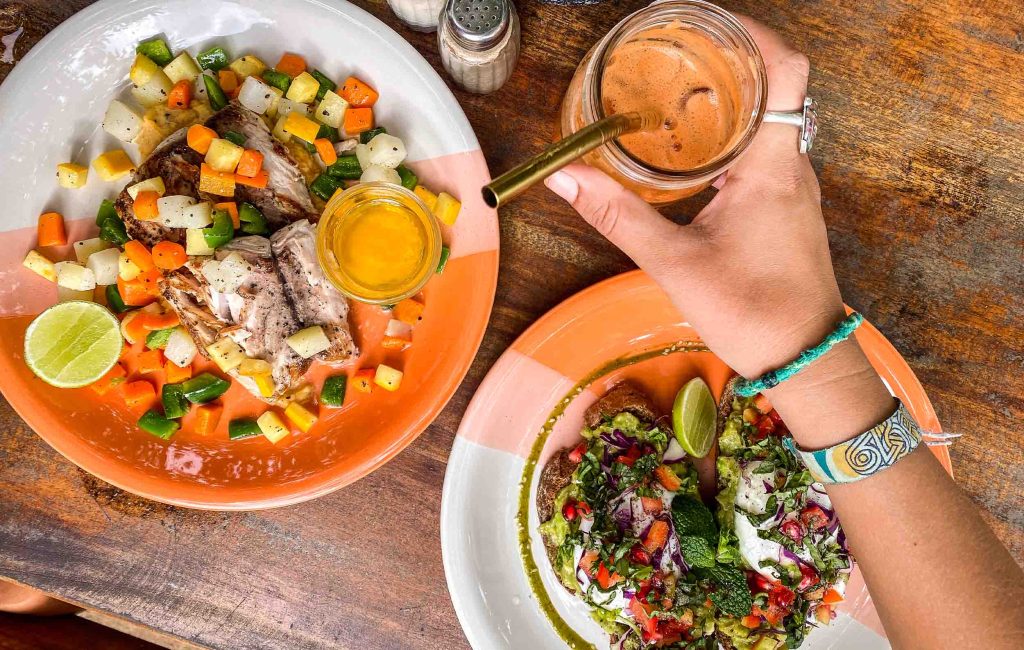 An overhead view of a colorful meal on a plate, with a refreshing drink on a rustic table, suggesting a tropical dining experience.