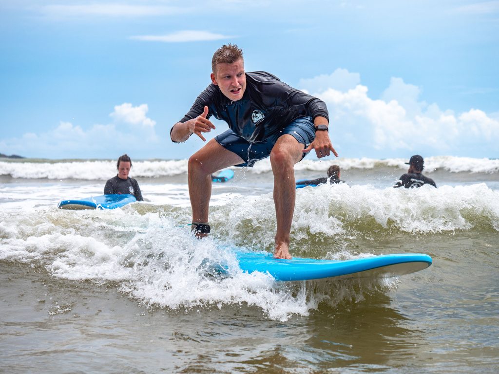 Male surfer skillfully riding a cresting wave under clear blue skies, embodying the thrill of water sports.