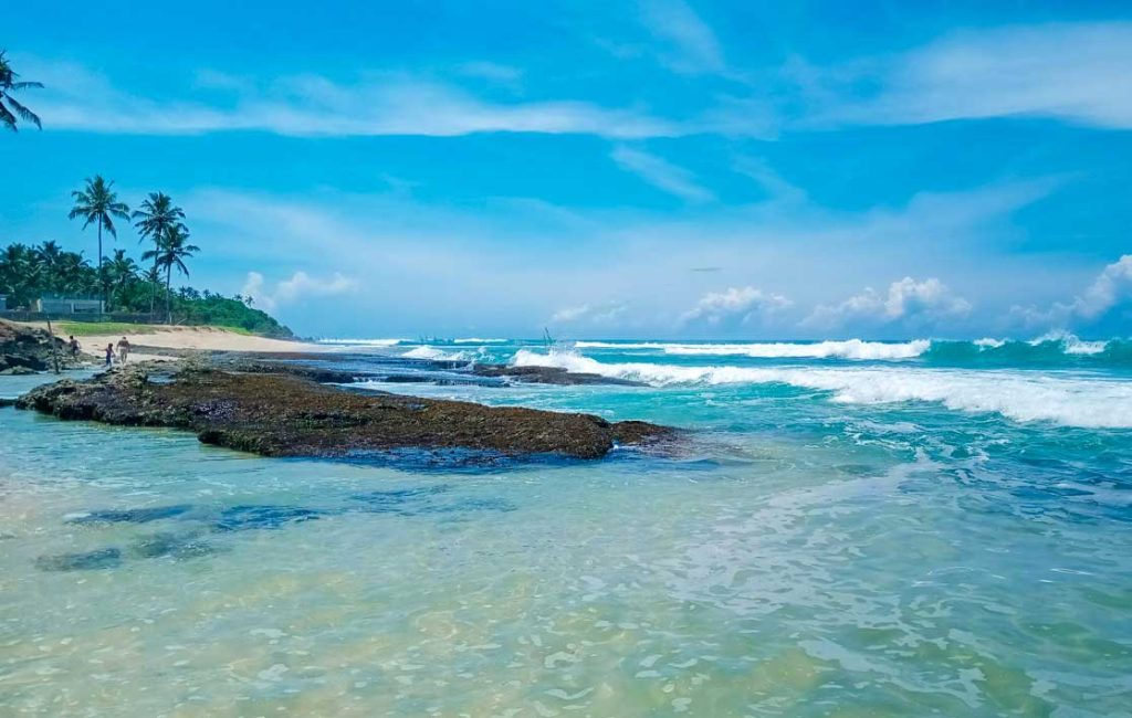 Idyllic seascape showing a rocky shore with clear blue waters and waves crashing, under a bright blue sky