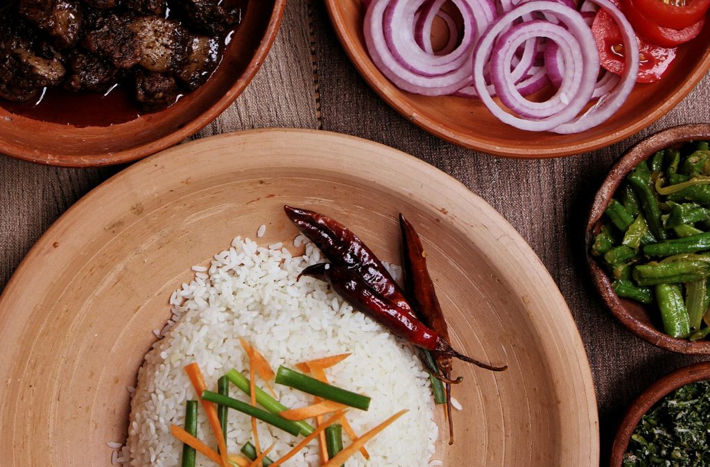 Traditional Sri Lankan meal served in earthenware dishes. The meal includes white rice, spicy beef curry, green beans, sliced onions, tomatoes, and a couple of red chilies on top