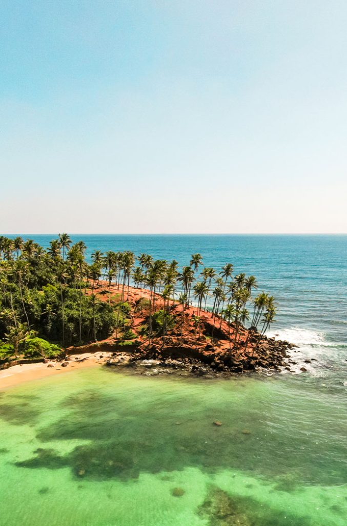 A panoramic view of a coastal landscape with a strip of beach, palm trees, and a calm turquoise sea extending to the horizon.