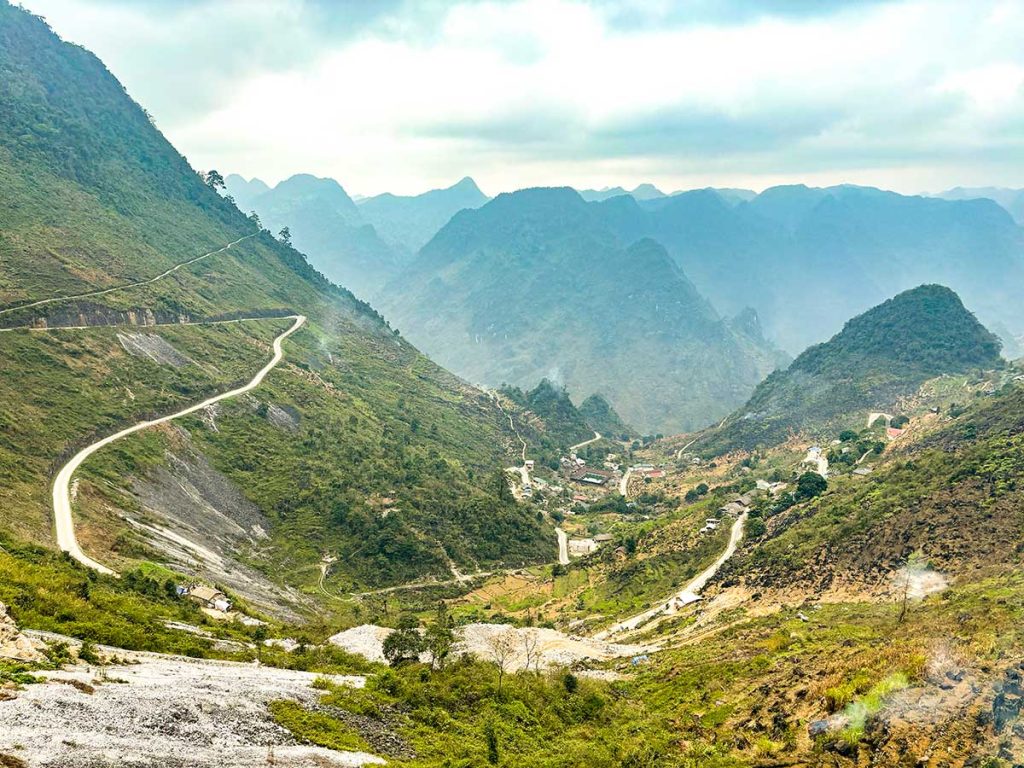 A picture of a winding road along the Ha Giang Loop with a small town settled in the valley. 