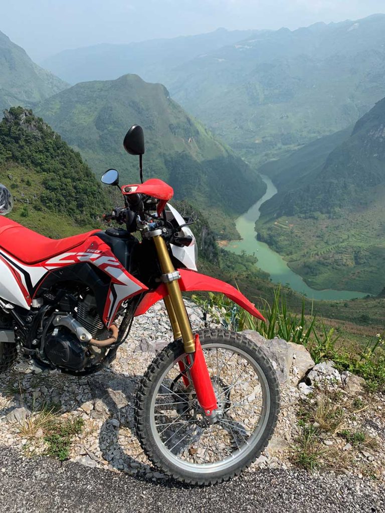 A picture of a bike parked at the side of a viewpoint looking down into a valley with a river