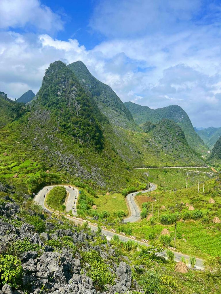 A road winding through a picturesque mountain landscape, with the sun casting long shadows over the hills. The road appears empty, offering a peaceful and solitary journey through nature.