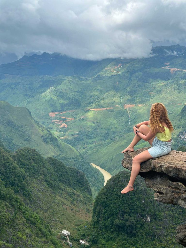 A picture of a woman sitting on a rock edge over a valley on the ha Giang Loop.