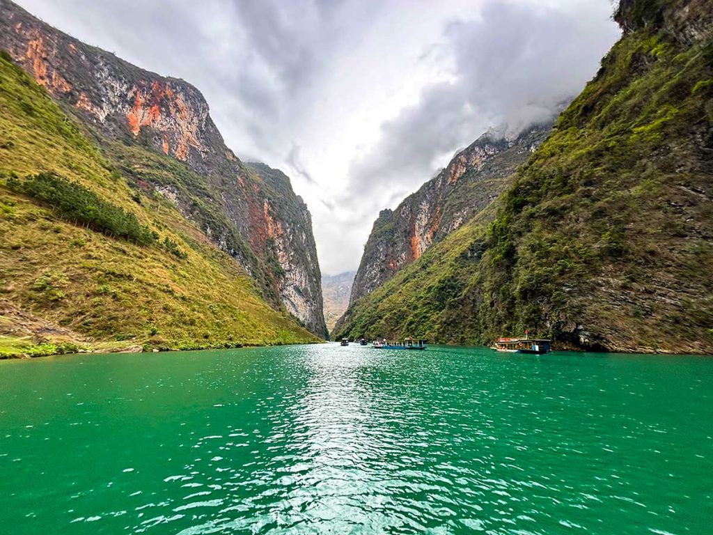 A  river winds through a deep valley, flanked by steep, green-covered mountains. The water appears calm and reflective, with mist hovering over the landscape, adding a sense of tranquility to the scene