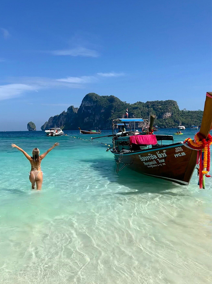 A woman posing beside a long tail boat in shallow water