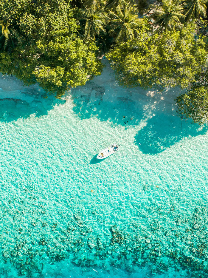 Aerial view of a small boat floating over crystal-clear turquoise water near a tropical shore.


