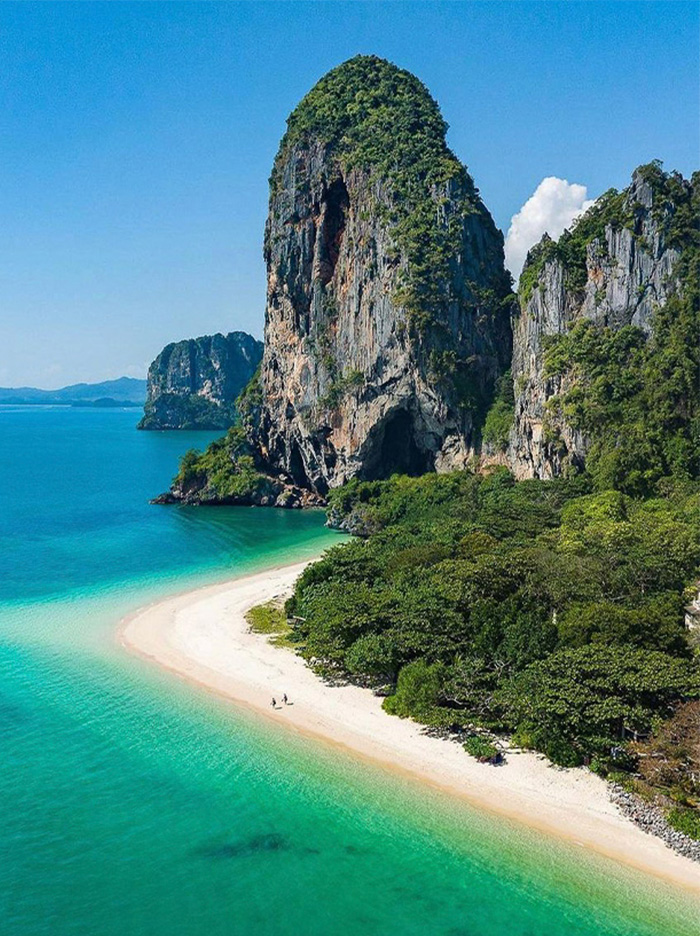 Limestone cliffs with greenery by the sea and sandy beach in Thailand