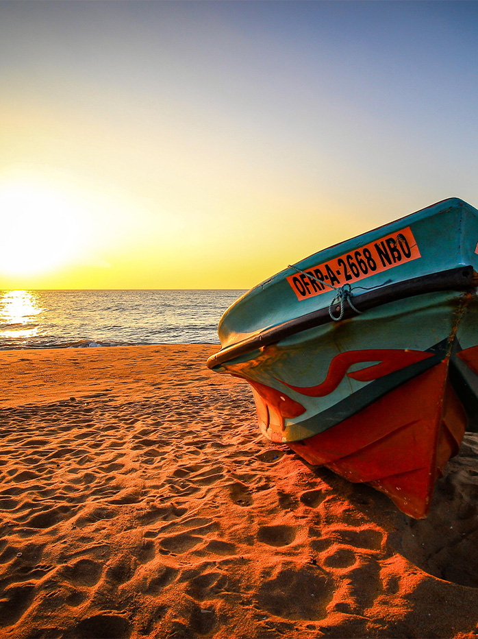 A fishing boat resting on the golden sands of a Sri Lankan beach during sunset.

