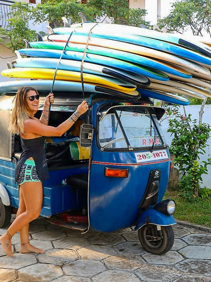 A woman securing surfboards on top of a blue tuk-tuk in Sri Lanka’s surf town.

