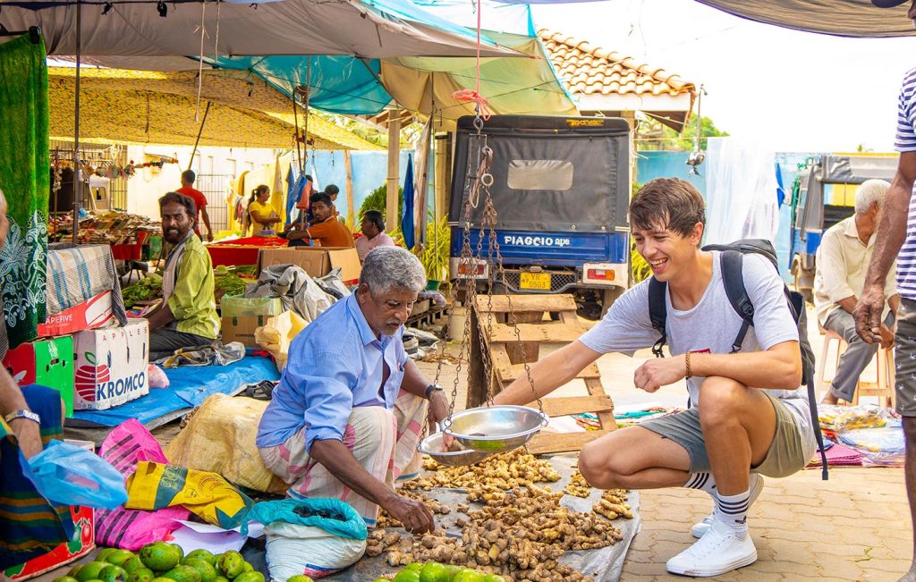 A smiling tourist buying fresh produce from a vendor at a vibrant Sri Lankan market.

