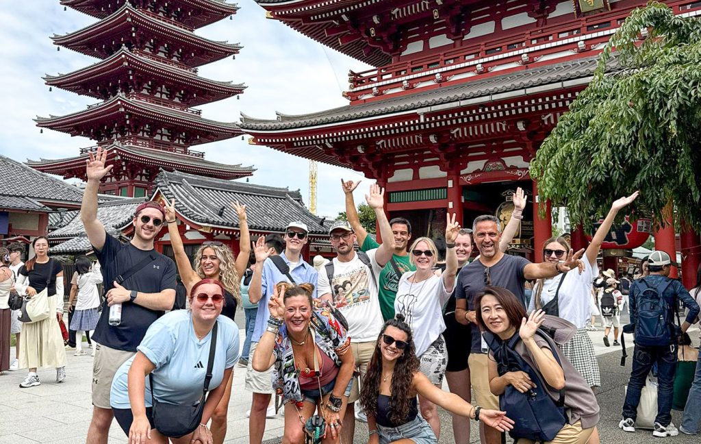 A group of tourists poses smiling in front of Sensō-ji Temple’s pagoda and gate in Tokyo.