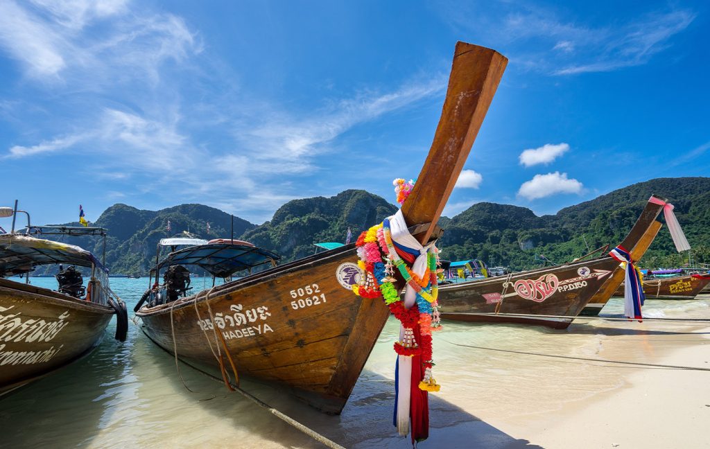 Traditional longtail boats decorated with colorful ribbons rest on a tropical beach.