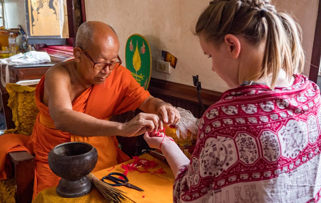 A monk ties a red bracelet on a woman’s wrist during a blessing ceremony.