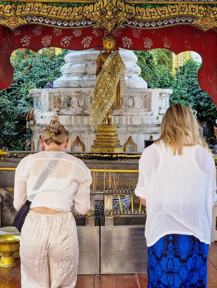 Two women stand in front of an ornate shrine, preparing to light incense.