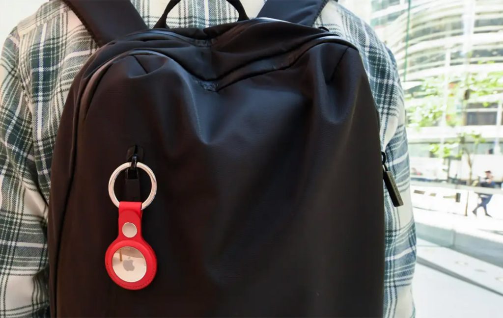 A black backpack features a red Apple AirTag keychain clipped to its strap.