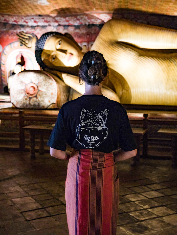 A woman stands before a reclining Buddha statue inside a temple.