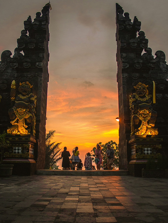 A group of tourists gathers beneath a dramatic temple gate at sunset.