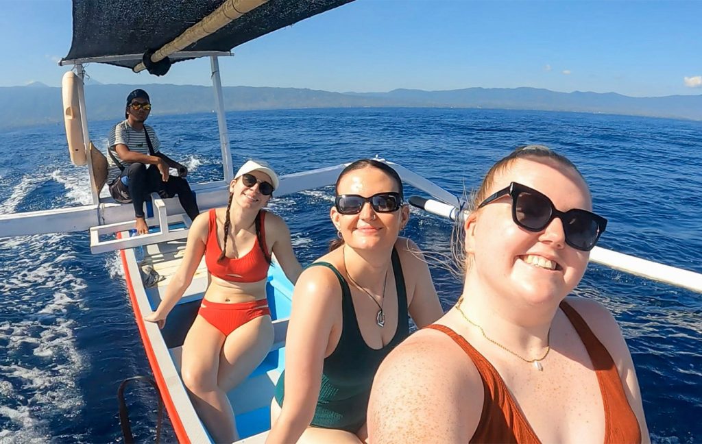 Three women in swimsuits smile for a selfie on a small boat with a guide at sea.