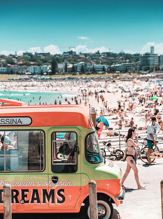 A colorful ice cream van parked by the busy Bondi Beach on a sunny day.