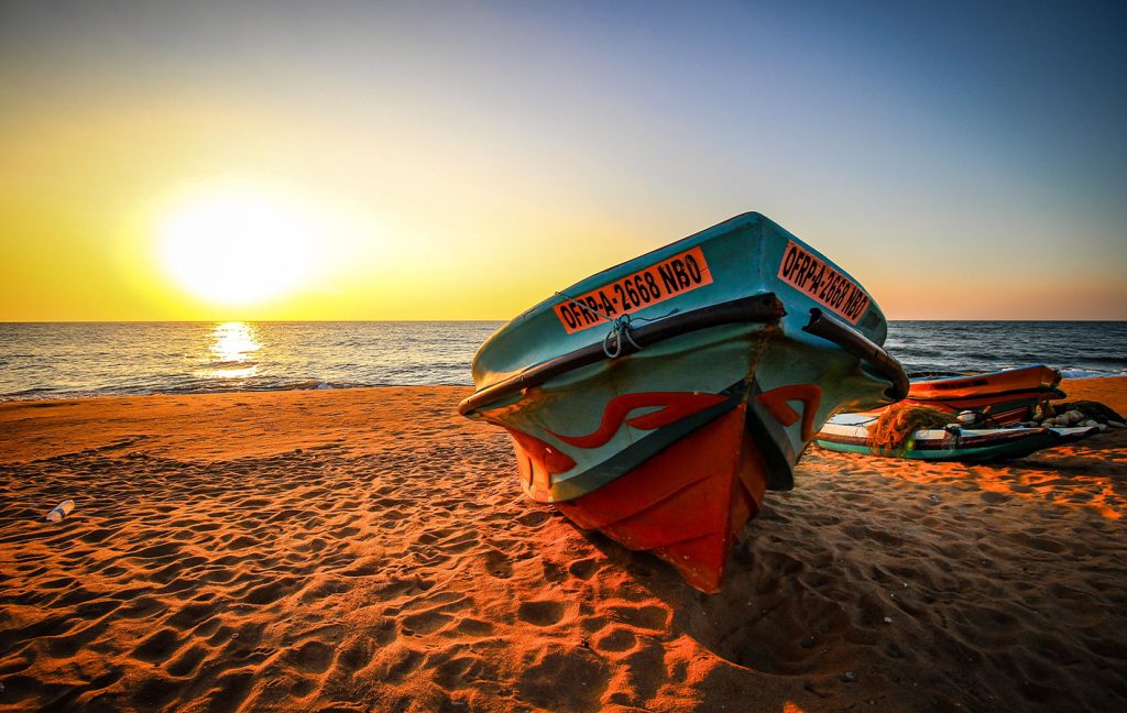 A colorful fishing boat rests on the sand at sunset by the sea.