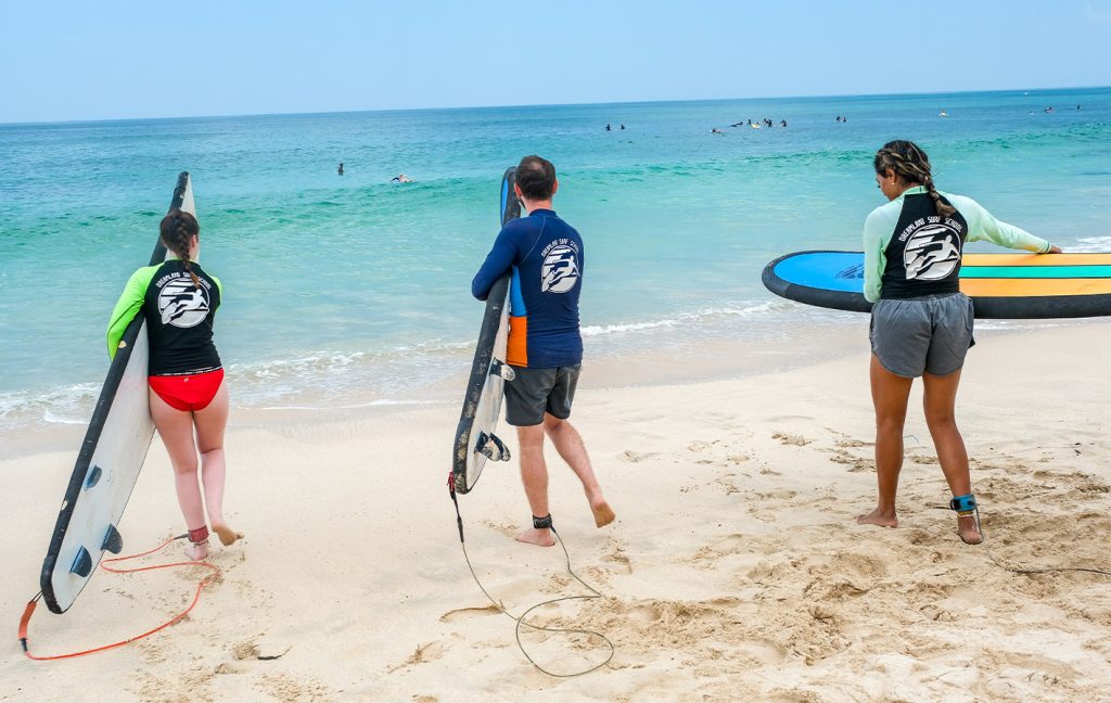 Three surfers carrying boards head toward the ocean waves.