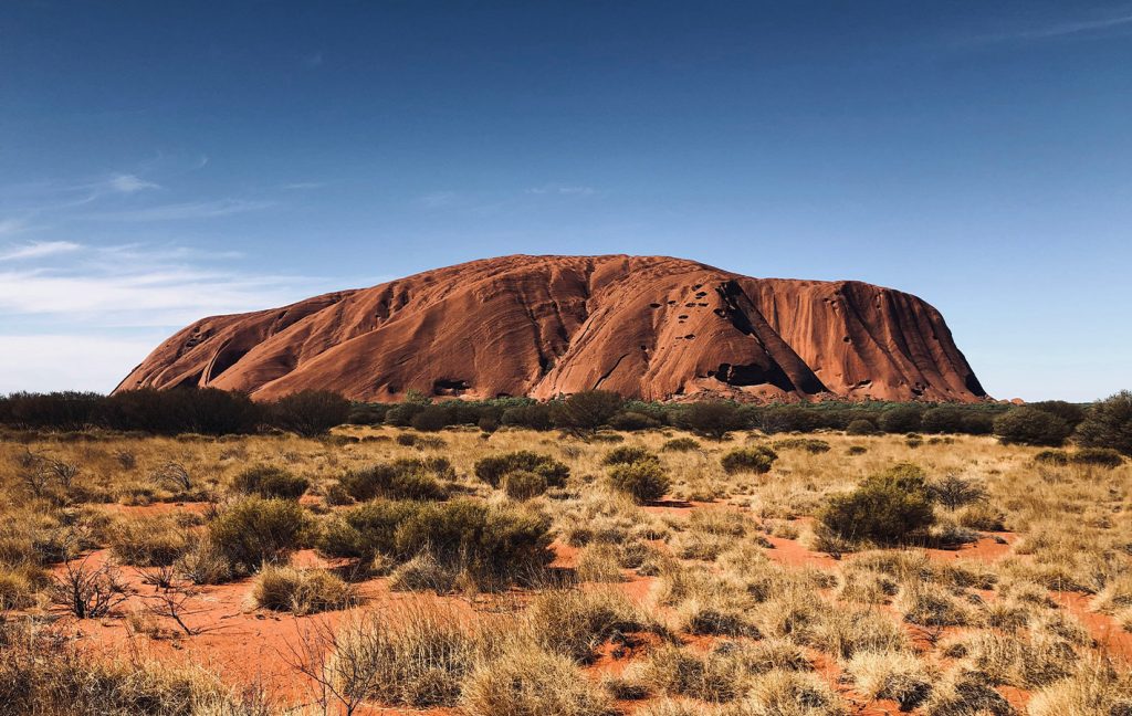 The iconic red rock formation of Uluru rises above the outback landscape.
