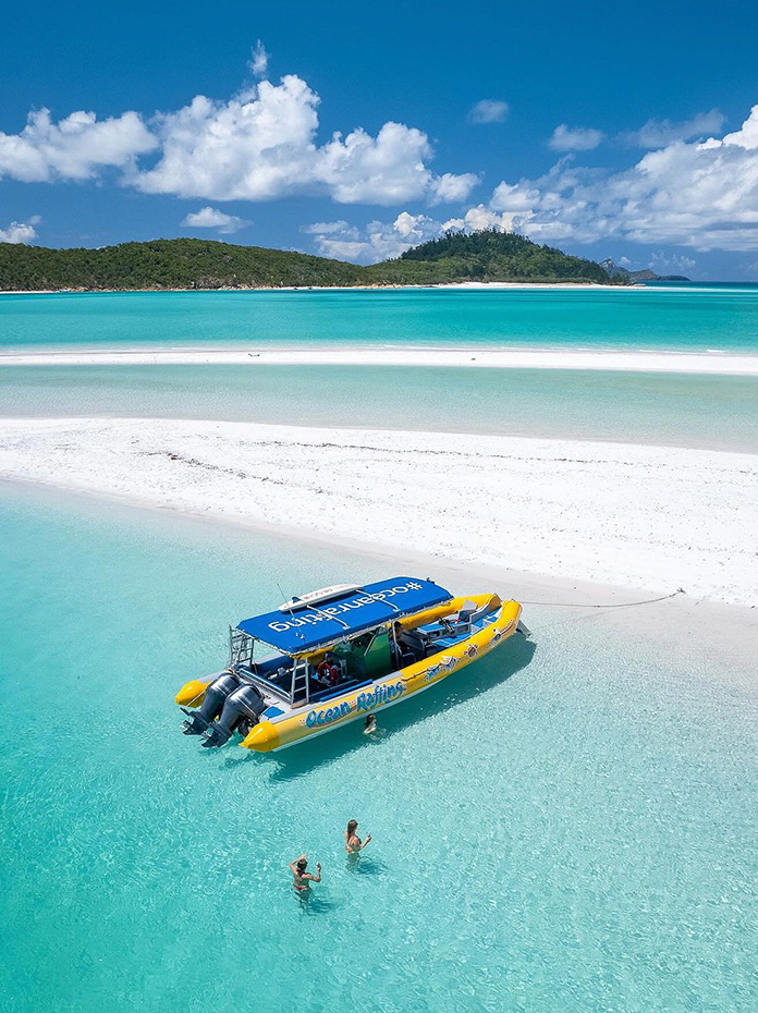 A yellow boat anchored in the crystal-clear waters near the white sands of Whitsundays.