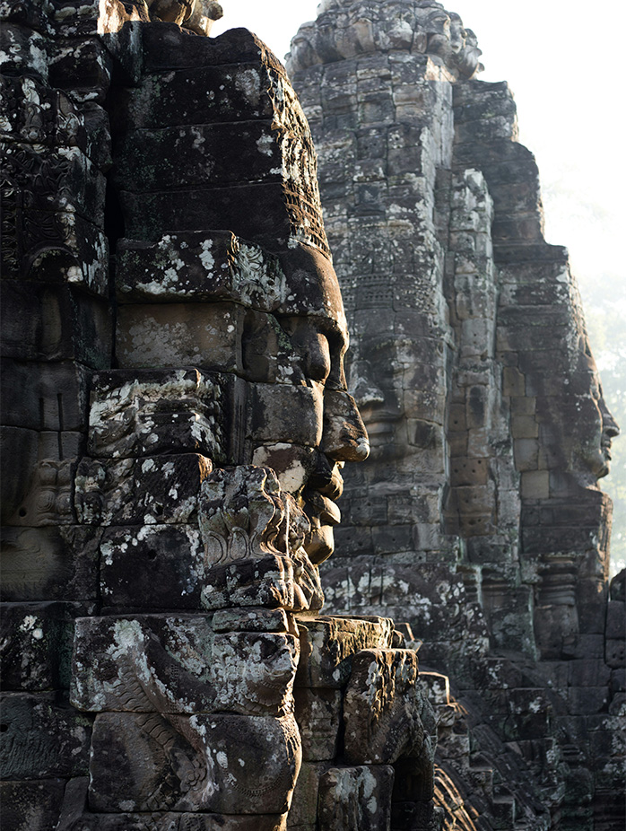 Ancient carved stone faces of Bayon Temple appear illuminated by soft natural light.